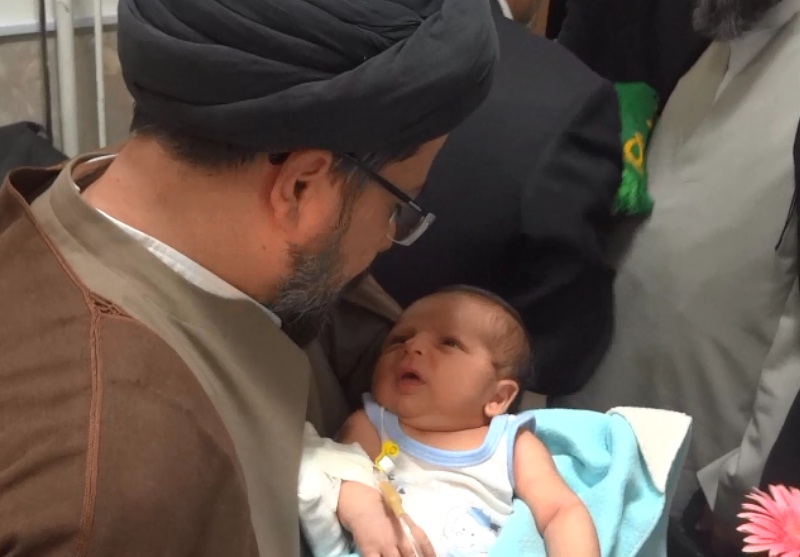 اذان خواندن روحانی کاروان خدام و پرچم متبرک حرم امام رضا(ع) در گوش نوزاد صحنه ای